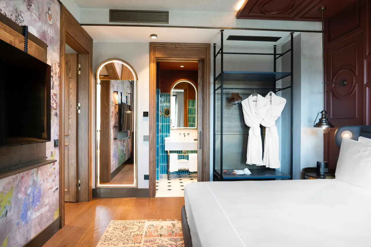Canopy by Hilton Istanbul Taksim’de modern tasarımlı bir otel odası; açık gardırop, ahşap zemin ve çağdaş banyo detayı.