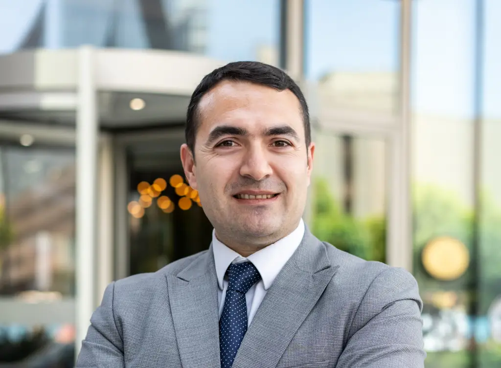 Veli Tolga Kahraman otel girişi önünde gri renkli takım elbisesiyle