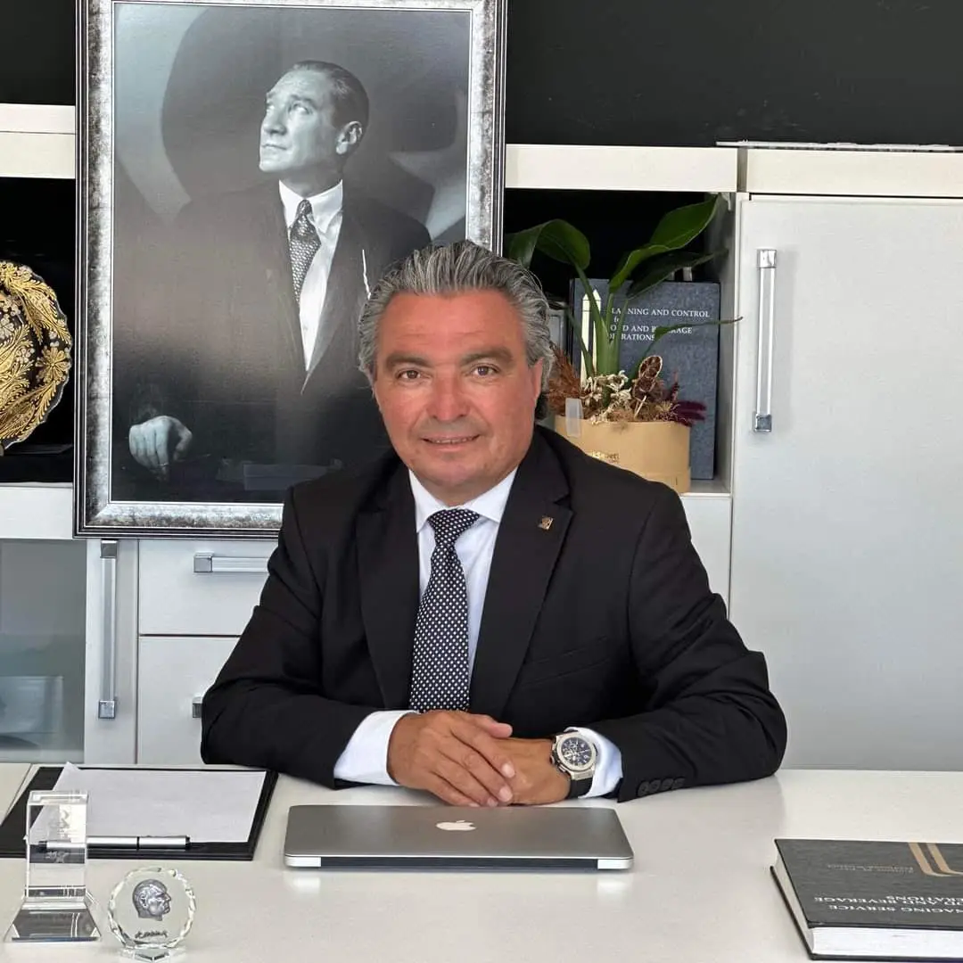 Ülkay Atmaca masasında otururken, arkada Atatürk portresi ile