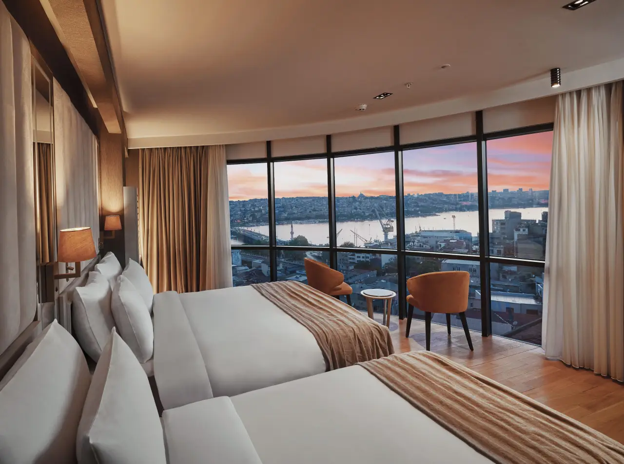 Otel odasında, geniş pencerelerden Haliç ve İstanbul manzarası eşliğinde iki adet rahat yatak.