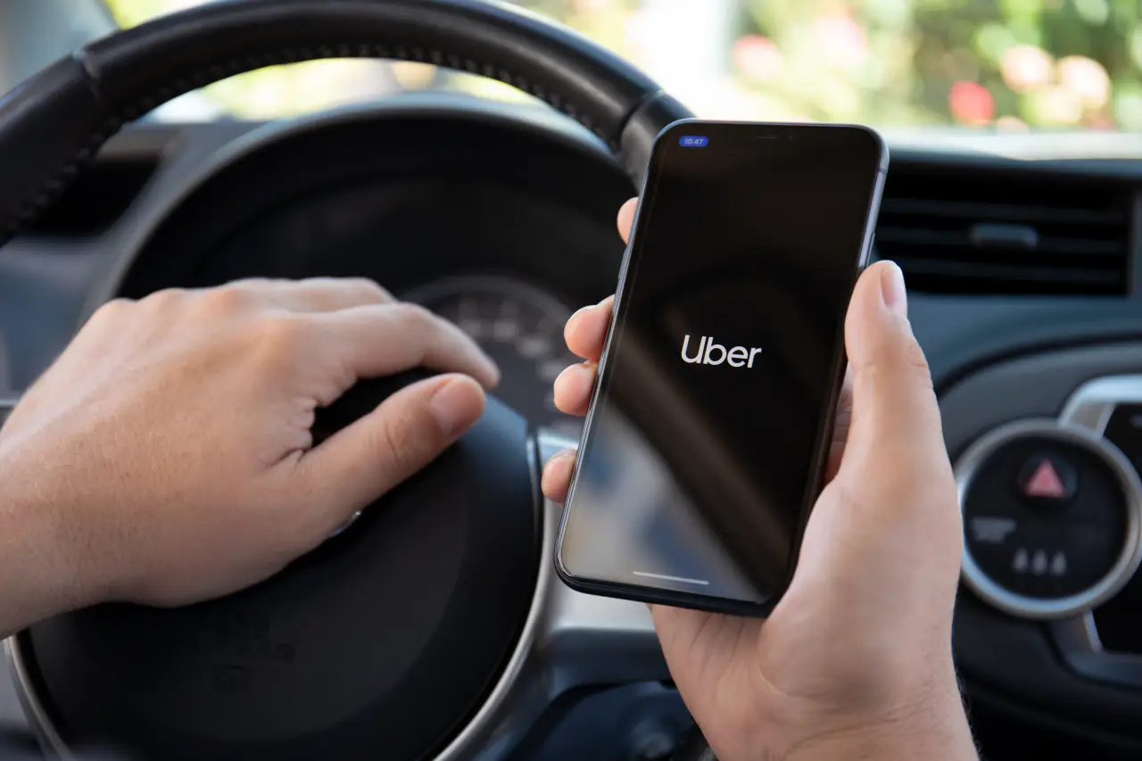 Direksiyon başındaki bir kişi, akıllı telefonunda Uber uygulamasını açmış.