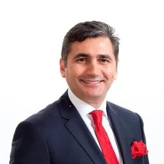 Kırmızı kravat ve mendil takan, koyu renk takım elbiseli, gülümseyen Emin Çakmak'ın portresi