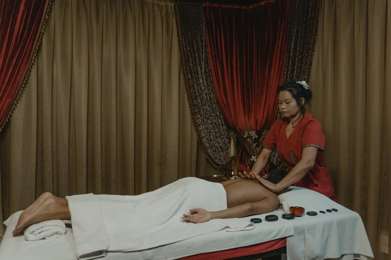 Geleneksel bir spa ortamında, kırmızı kıyafetli terapist masaj yapıyor.
