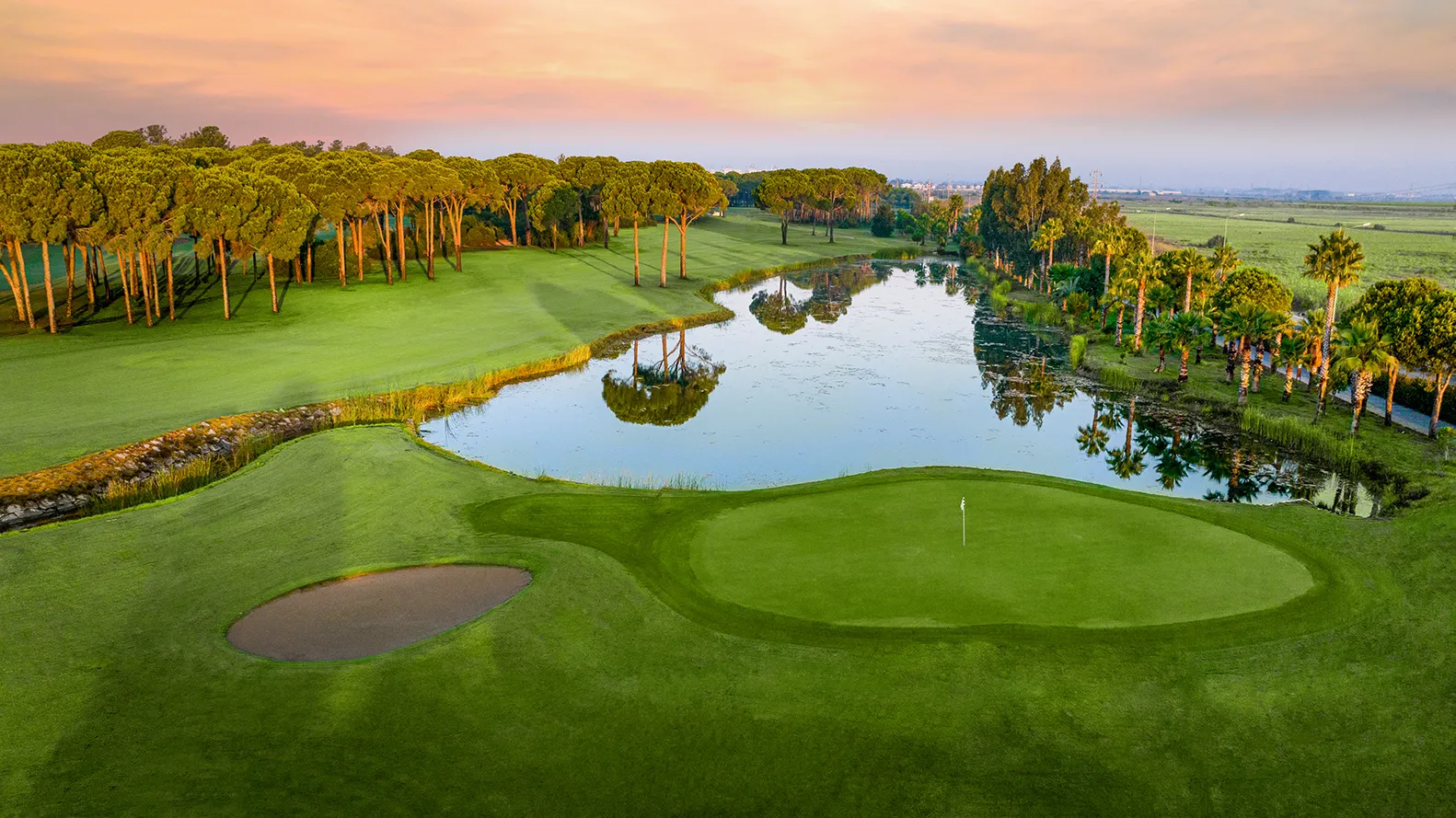Gloria Golf Club sahasında gün batımında gölet ve golf alanı manzarası