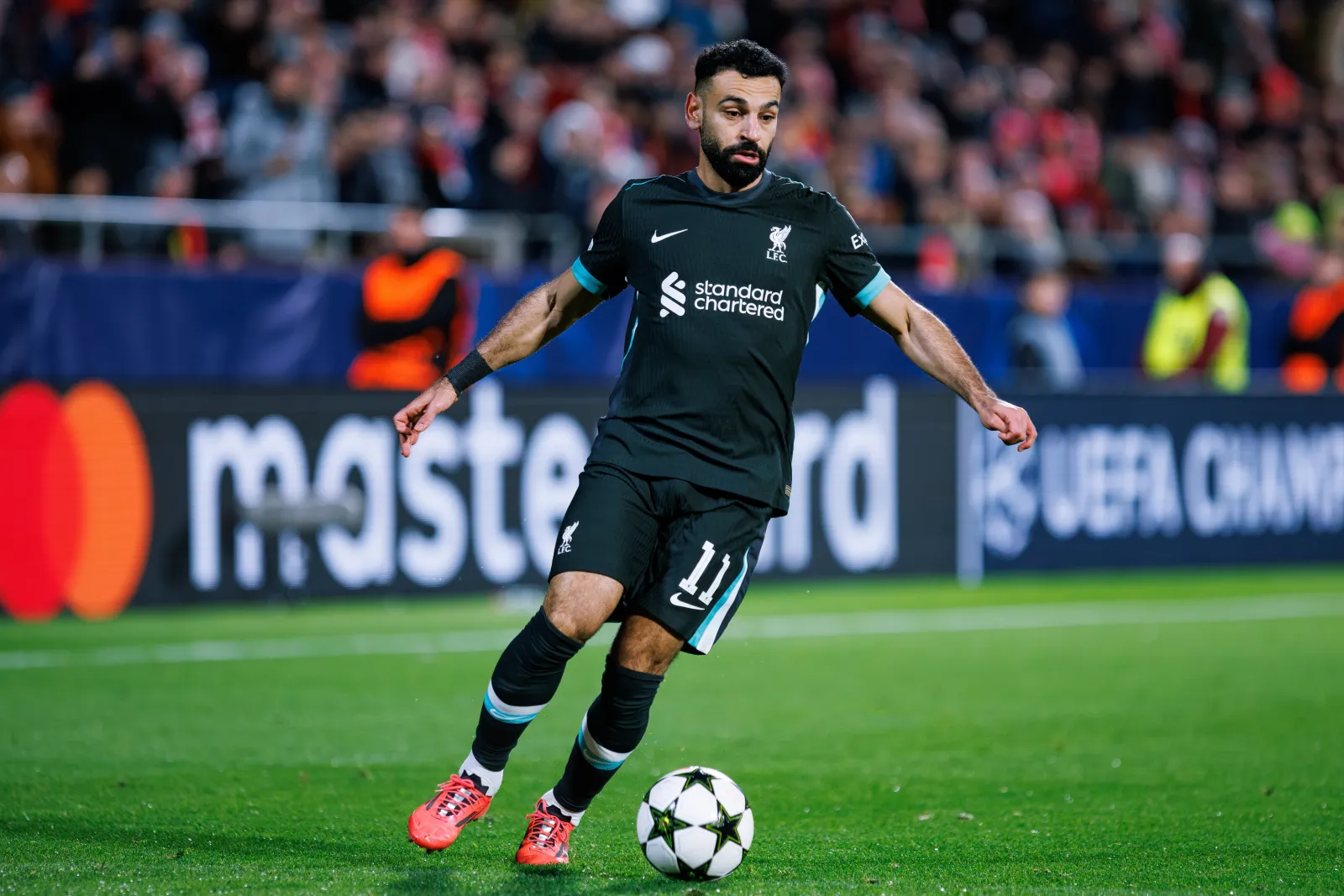 Liverpool formasıyla Mohamed Salah, UEFA Şampiyonlar Ligi maçında top sürerken sahada odaklanmış şekilde görülüyor.
