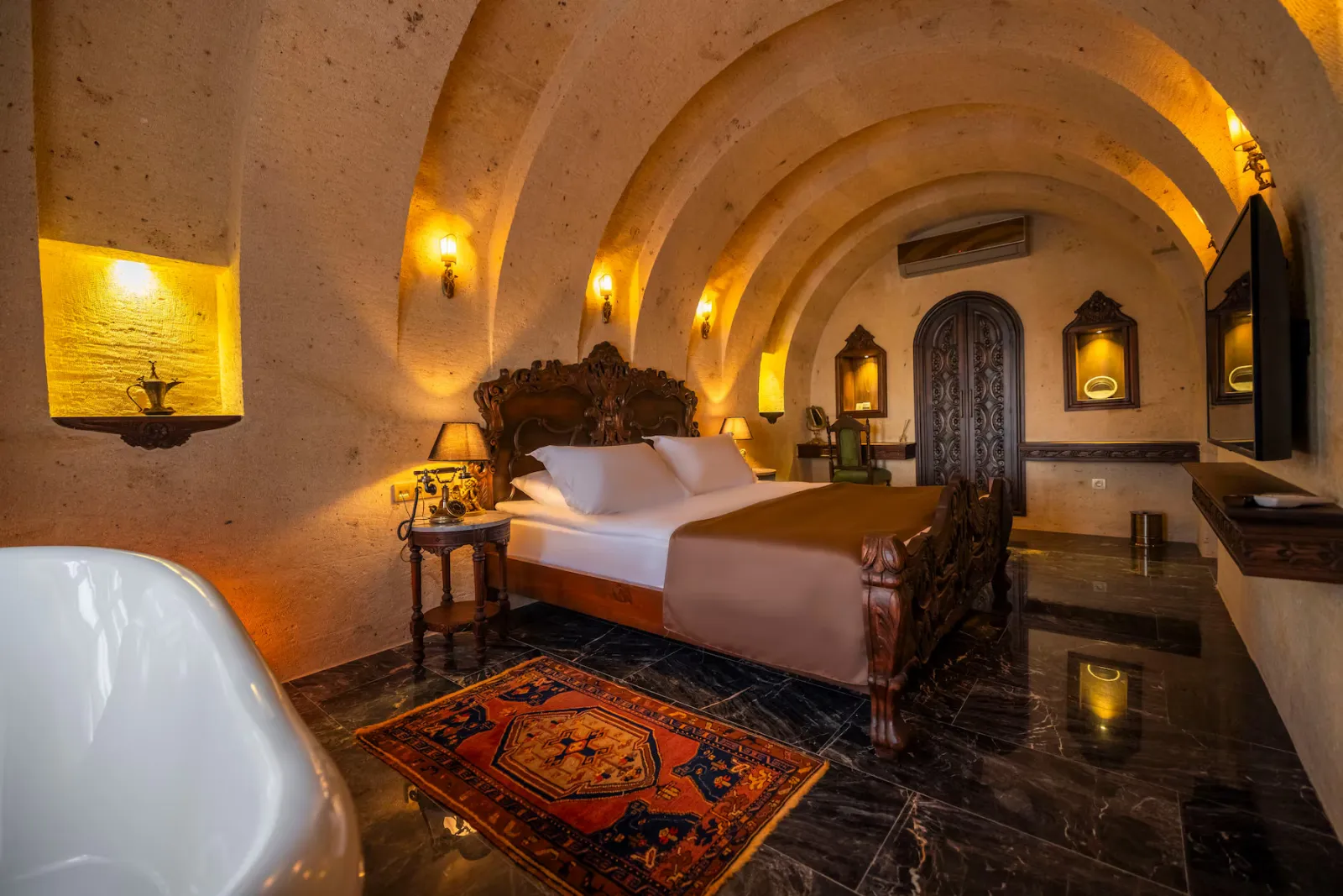 Signature Cave Cappadocia otel odası, taş kemerli tavanlar, antika mobilyalar ve sıcak aydınlatmasıyla Kapadokya’nın mağara konaklama deneyimini yansıtıyor.