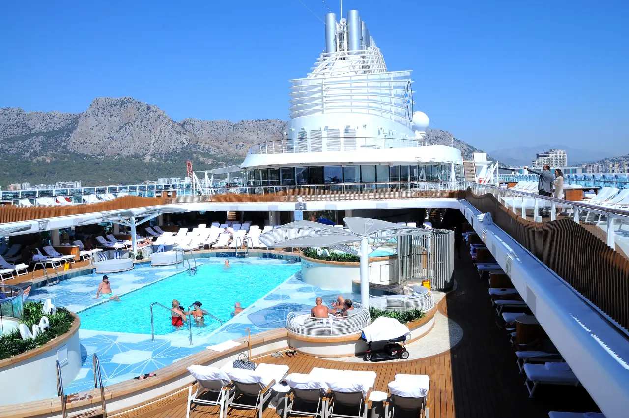 MV Allura kruvaziyer gemisinin güvertesinde havuz ve dinlenen yolcular, arka planda Antalya manzarası