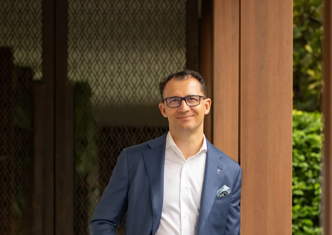 Khun Antonio Saponara, General Manager of Capella Bangkok, in a blue suit standing by a wooden wall