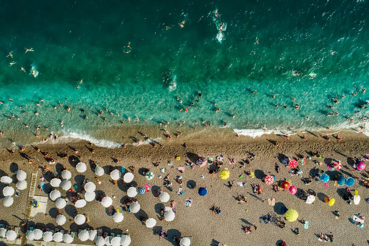 Havadan çekilmiş kalabalık bir plajda denize giren insanlar ve renkli şemsiyeler