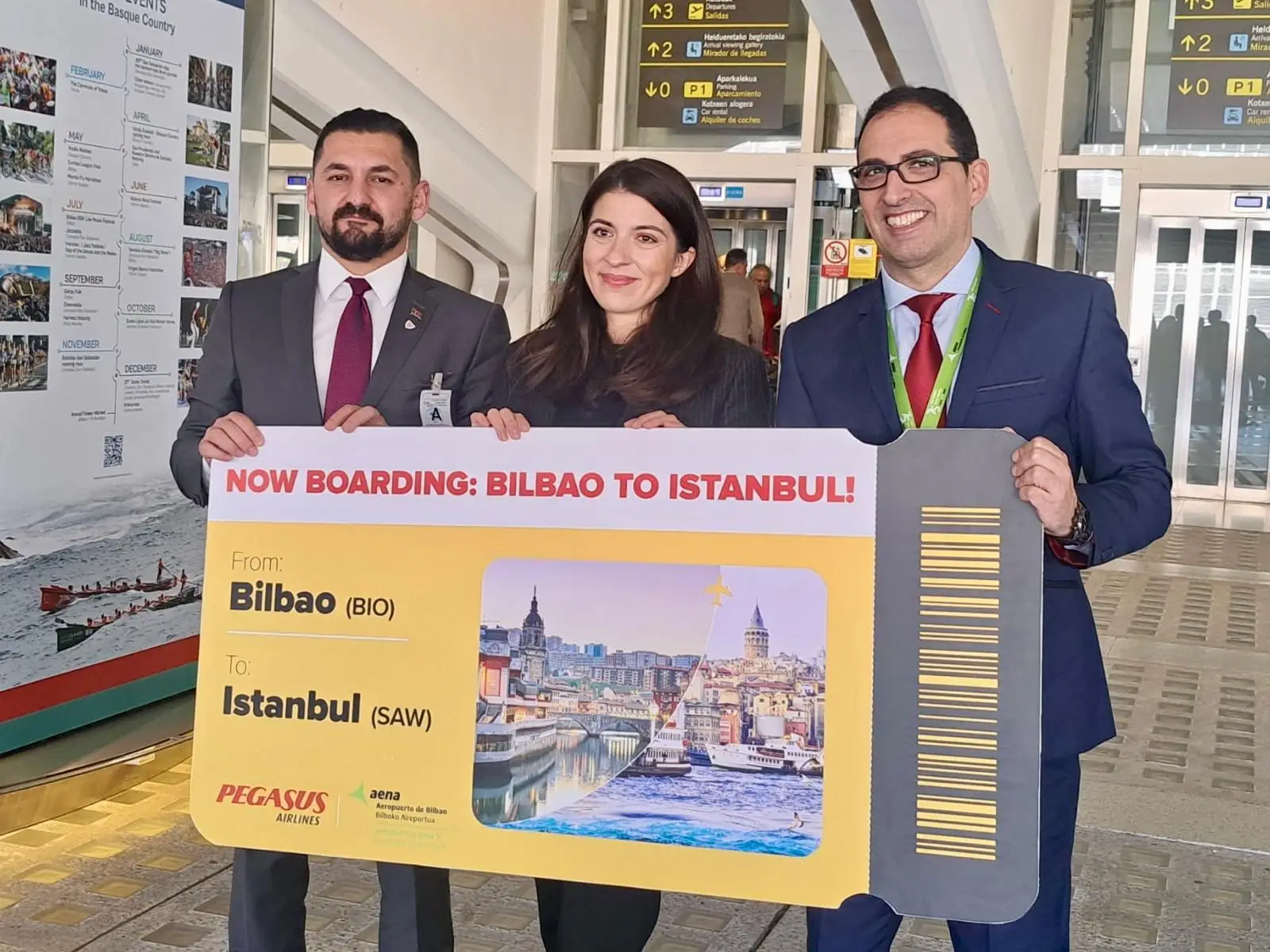 Bilbao Havalimanı’nda Pegasus’un İstanbul uçuşu için tören pozu veren üç yetkili, büyük bir sembolik biniş kartı tutuyor.