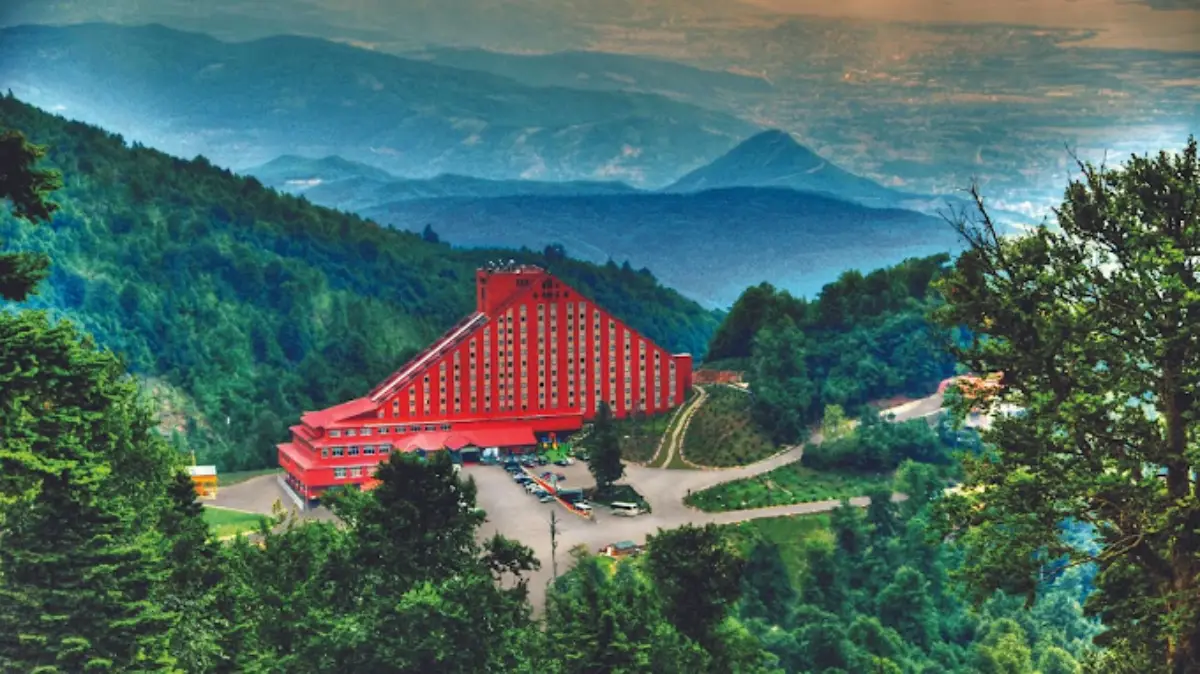 Kartepe’nin ormanlık dağ manzarası içinde, zirvede yer alan kırmızı renkli The Green Park Kartepe Resort Oteli’nin havadan görünümü.