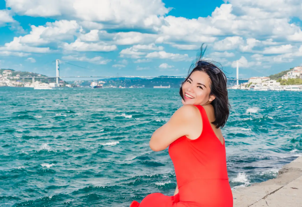 Boğaz kıyısında, arka planda köprü manzarasıyla poz veren Çinli kadın turist