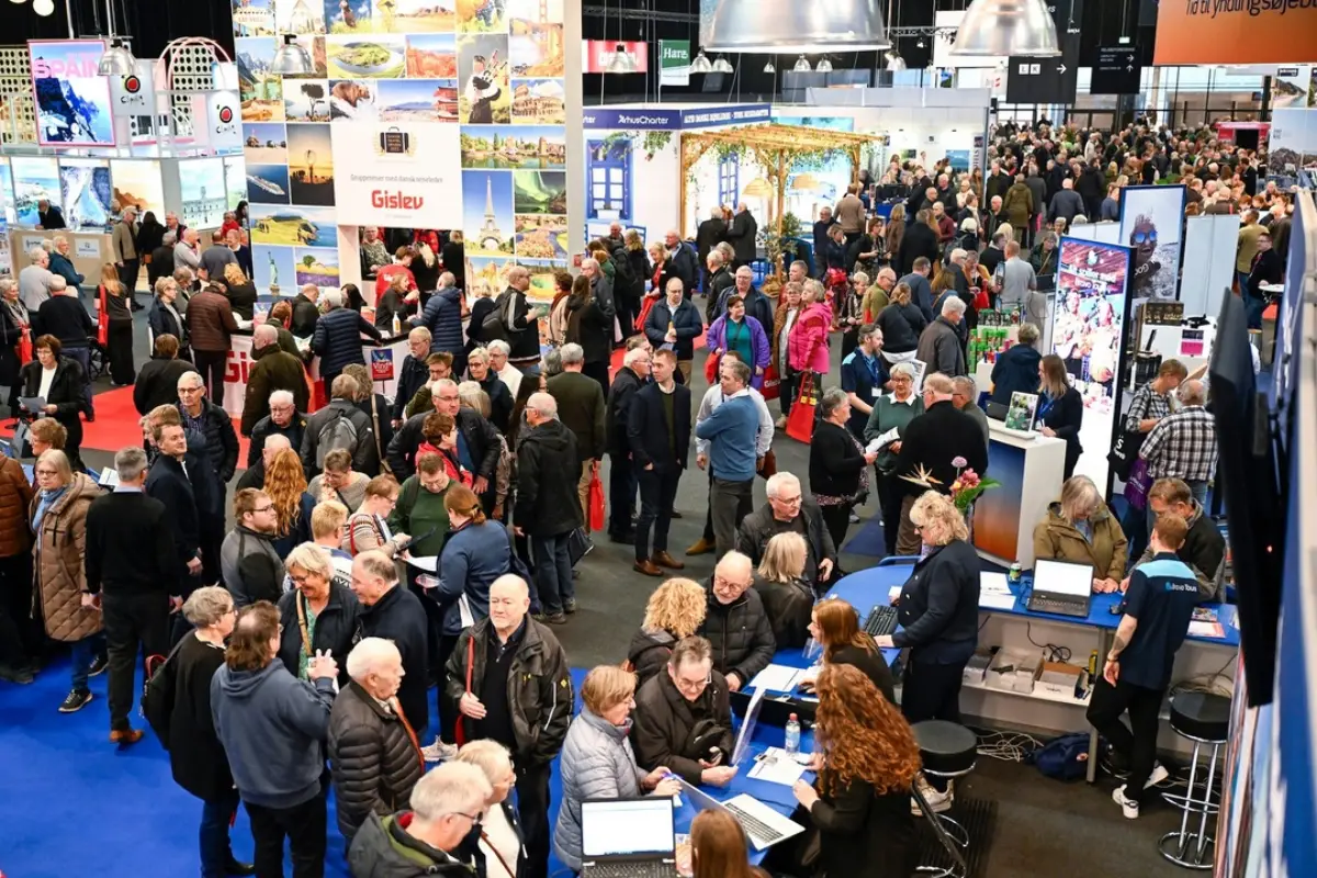 Kalabalık bir turizm fuarı salonunda, Herning’deki Ferie for Alle etkinliğinde yer alan destinasyon stantları ve ziyaretçiler