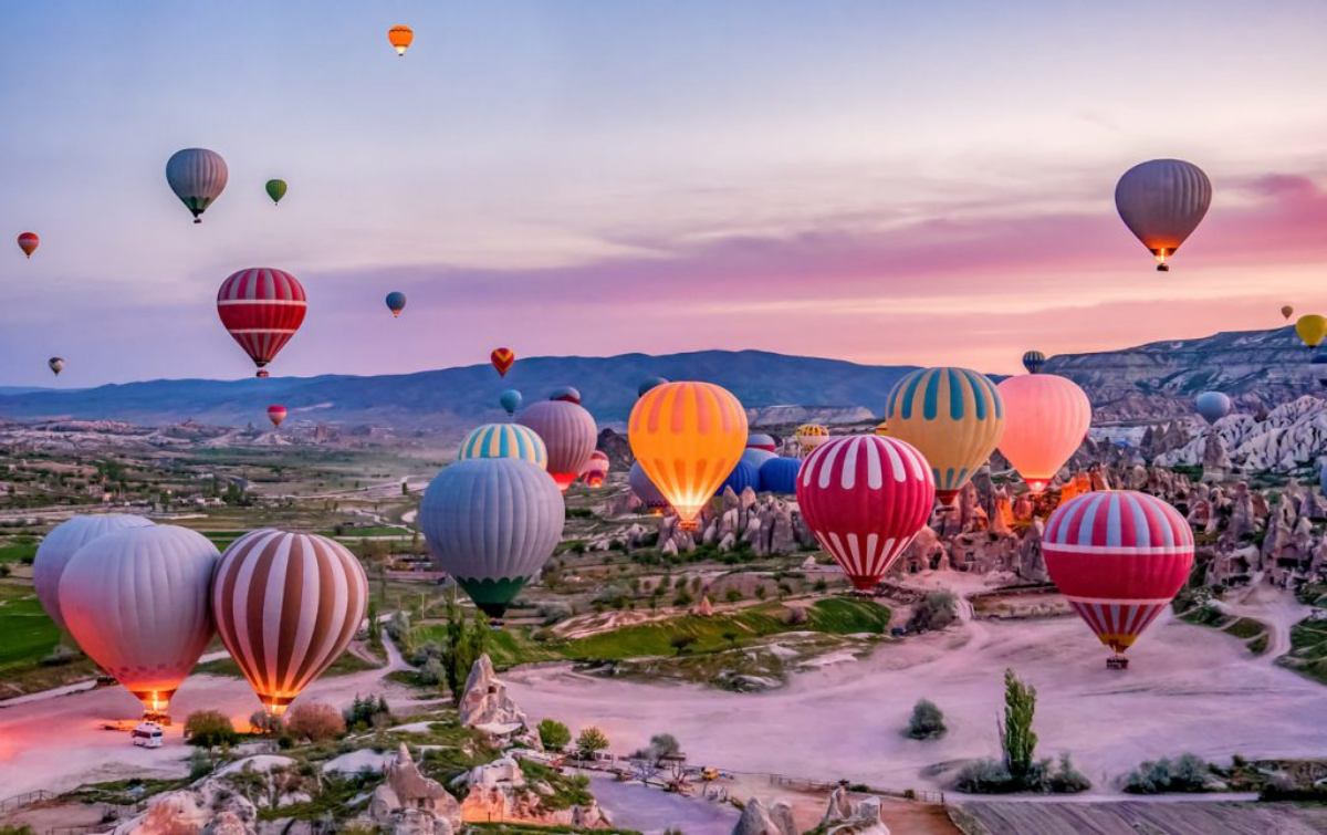 Kapadokya’da gün doğumunda peri bacaları üzerinde yükselen renkli sıcak hava balonları.