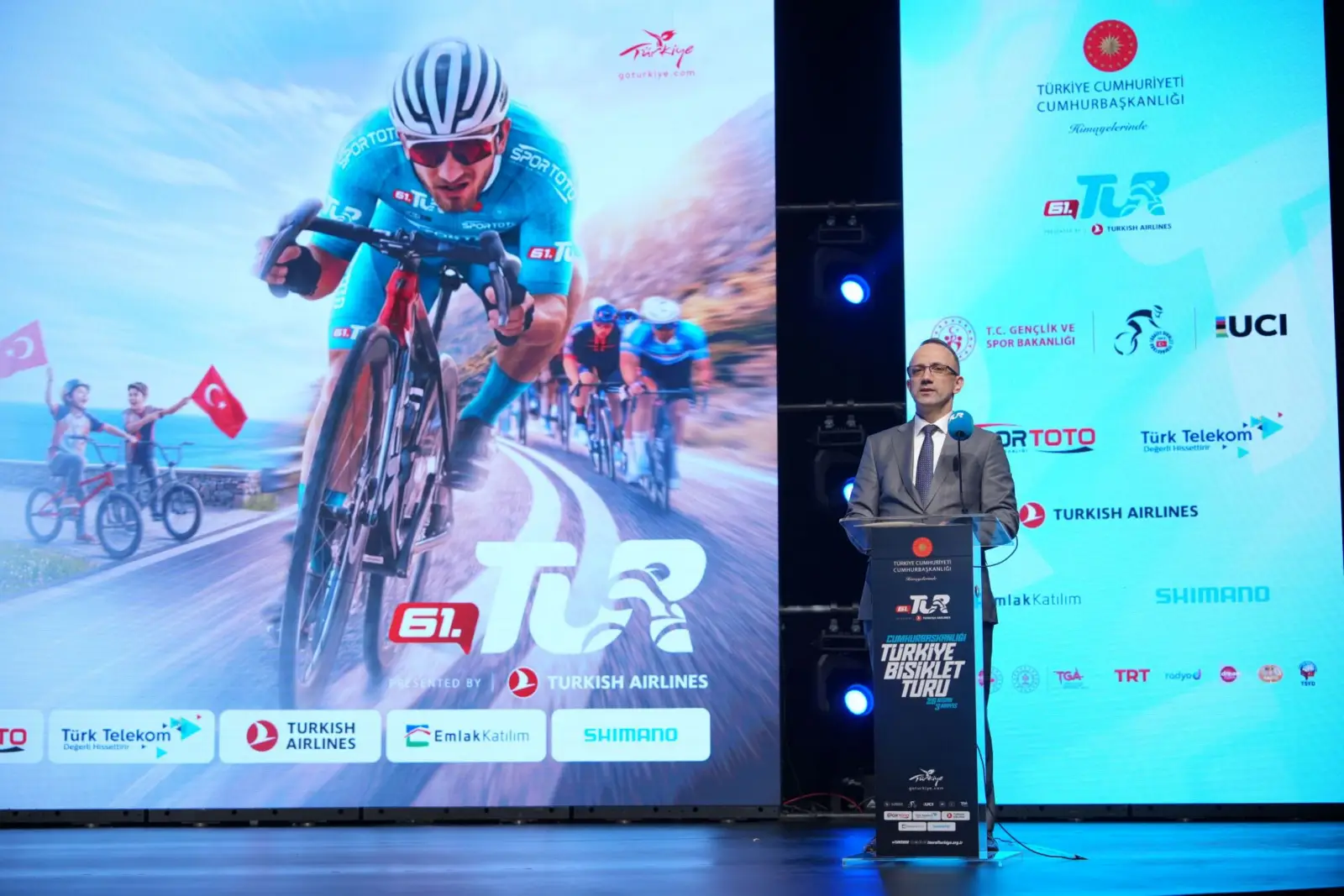Cumhurbaşkanlığı Türkiye Bisiklet Turu 2026 tanıtım toplantısında konuşma yapan yetkili ve arka planda yarış görselleri