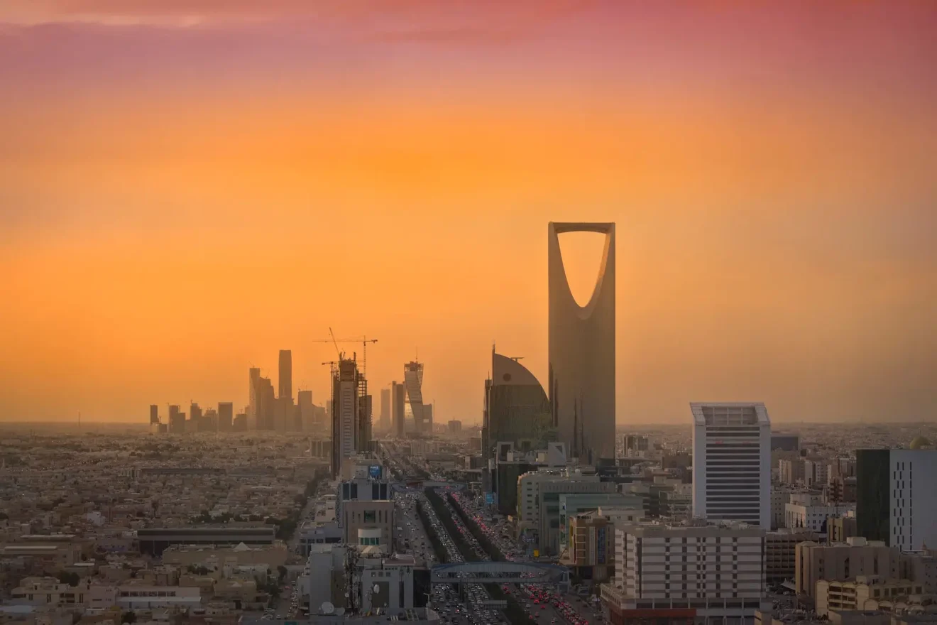 Riyadh skyline at sunset with Kingdom Centre Tower prominent against an orange sky
