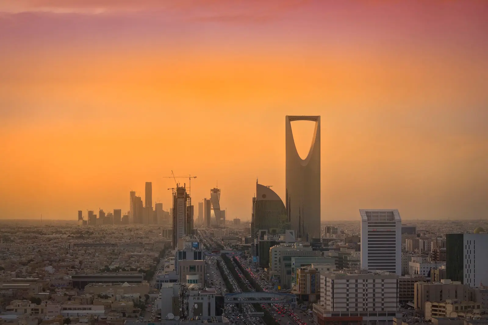 Riyadh skyline at sunset with Kingdom Centre Tower prominent against an orange sky