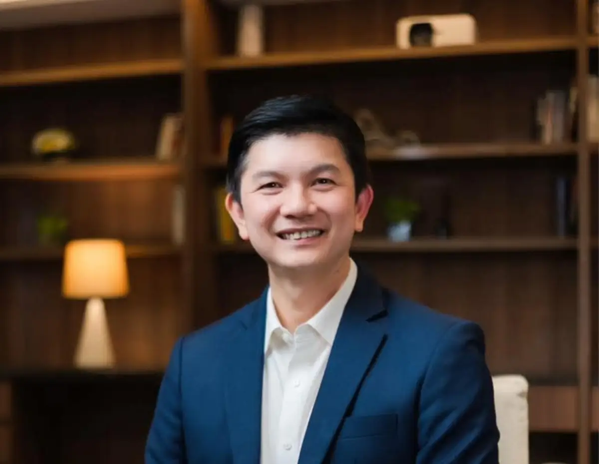Thanatouch Kaiwannon, General Manager of Prince Palace Hotel Bangkok, smiling in a professional portrait taken in a warmly lit office setting with wooden bookshelves in the background.