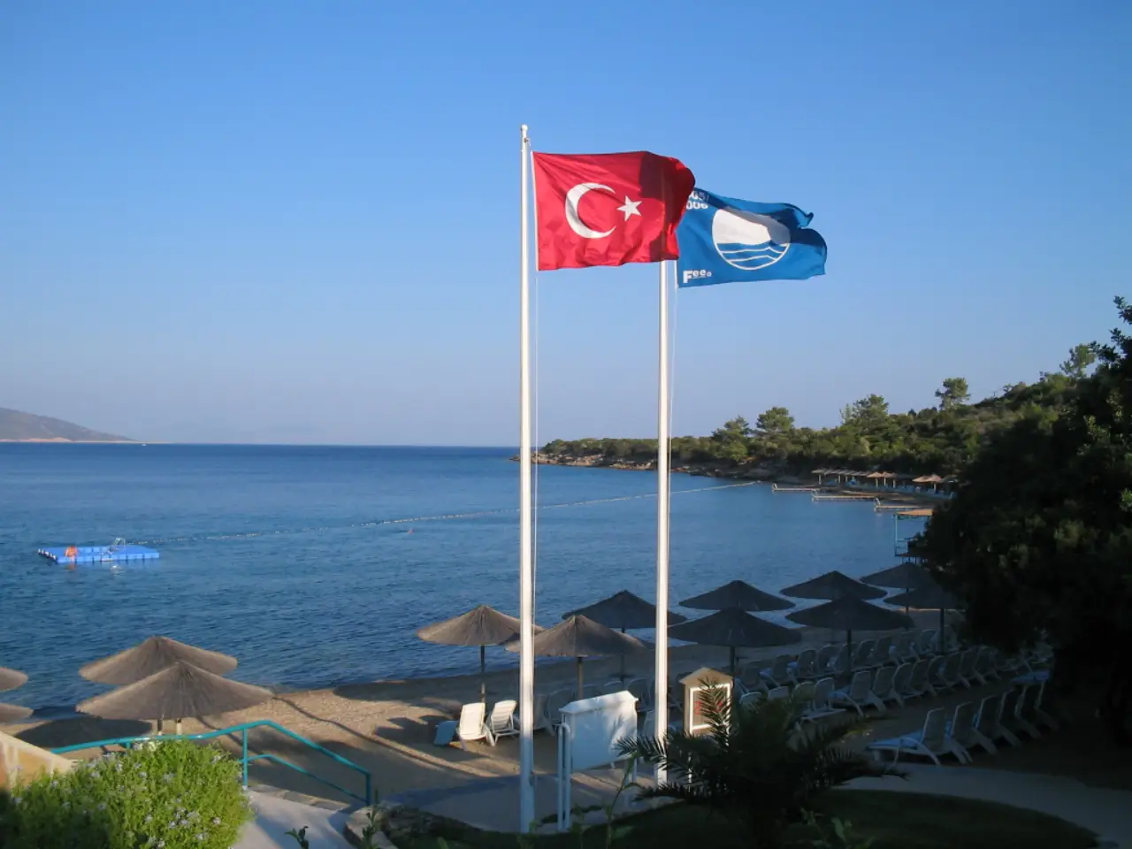 Türkiye’de Mavi Bayrak ödüllü bir plajda Türk bayrağı ve Mavi Bayrak bayrağı deniz kıyısında dalgalanıyor.