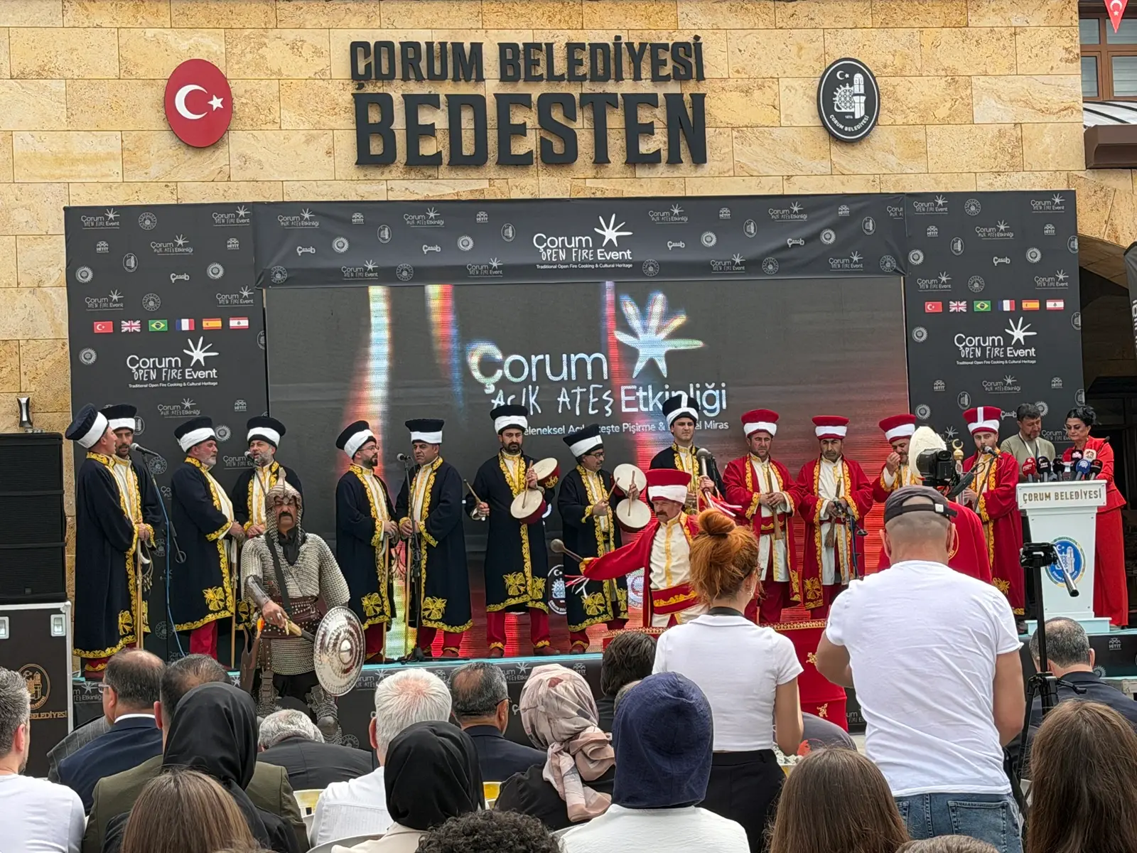 Çorum Belediyesi Bedesten önündeki sahnede geleneksel kıyafetlerle performans sergileyen mehter takımı ve önünde oturan kalabalık izleyici topluluğu