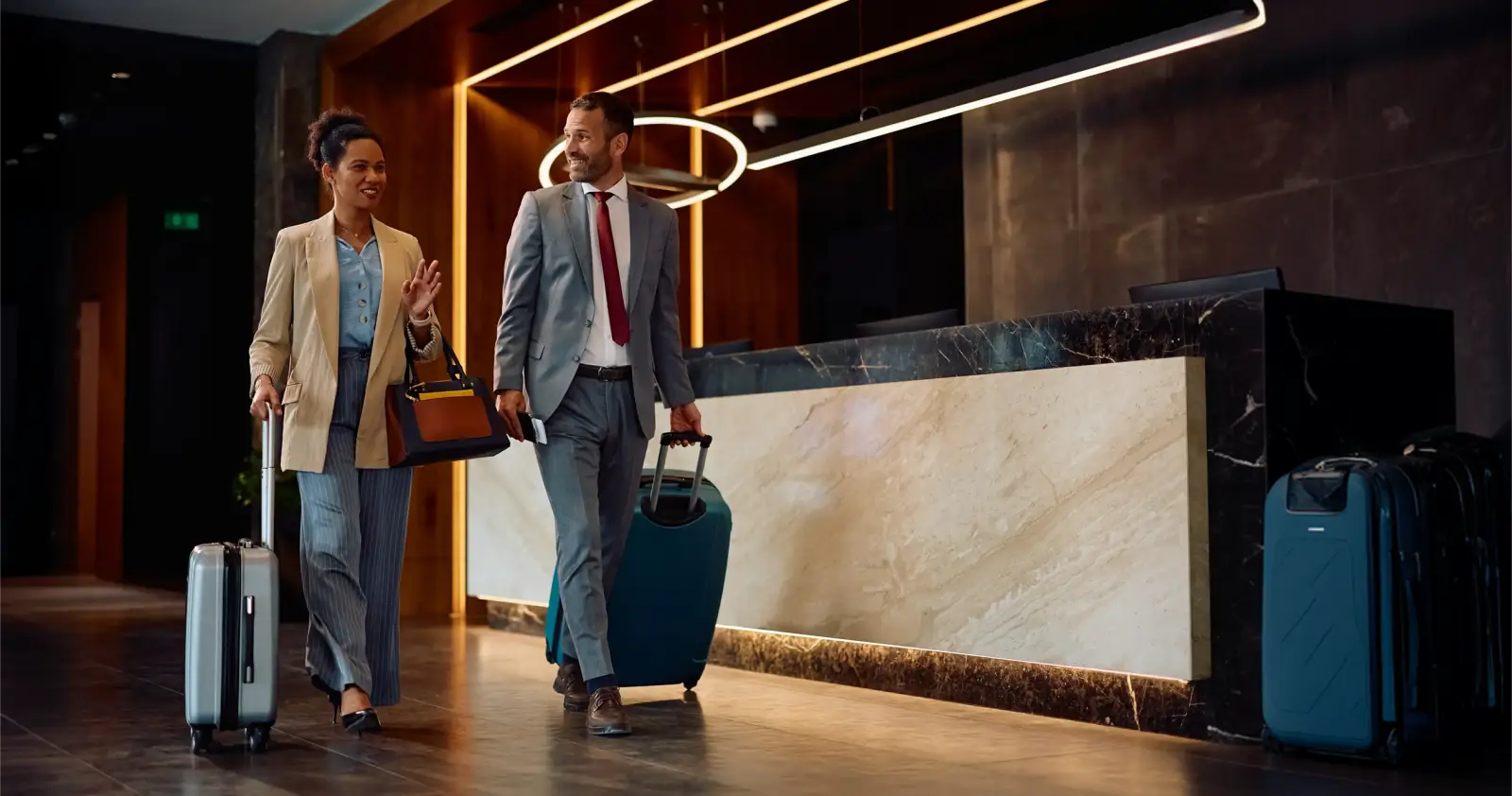 İş seyahatçileri otel lobisinde bavullarıyla check-in'e gidiyor