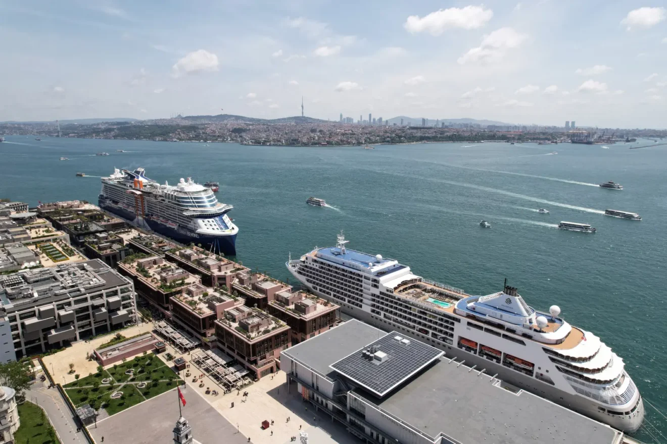 Galataport İstanbul'da rıhtıma yanaşmış iki büyük kruvaziyer gemisinin havadan görünümü, arka planda İstanbul Boğazı, vapurlar ve kent silueti yer alıyor