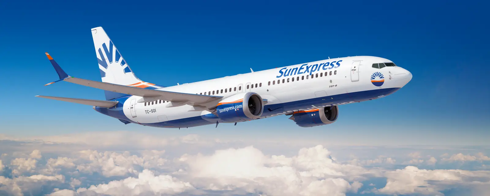 SunExpress'in beyaz ve mavi renkli Boeing 737-8 uçağının mavi gökyüzünde ve bulutların üzerinde uçarken çekilmiş yan görünümü